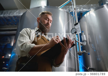 Handsome bearded man brewer inside modern beer factory around steel tanks 98801789