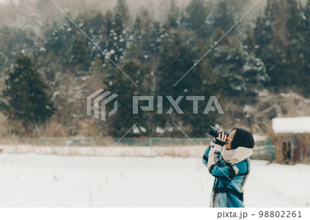 雪の中若い女性がカメラを持っている写真 98802261