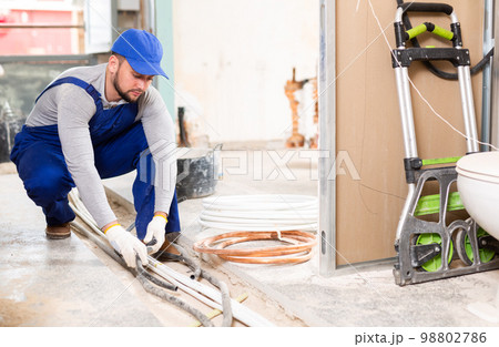 Man electrical installer laying cables through trench Man electrical installer laying cables through trench 98802786