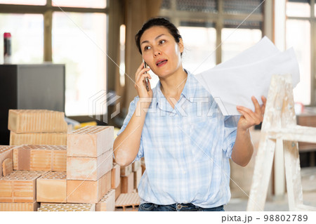Woman architect is talking on the mobile phone, studying documents Woman architect is talking on the mobile phone, studying documents 98802789