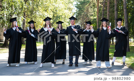 Group of graduates in robes dancing outdoors. Elderly student. Group of graduates in robes dancing outdoors. Elderly student. 98802980