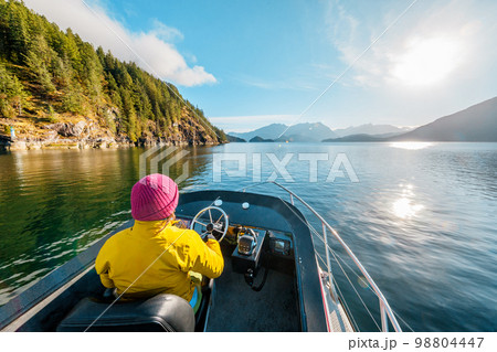 Woman Driving Motor Boat in Amazing Nature Landscape at Sunset in Coastal British Columbia Near Bute, Toba Inlet and Campbell River. Whale Watching Tourist Travel Destination, Canada 98804447