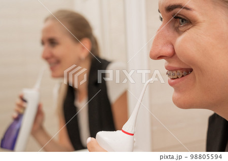 A woman with braces on her teeth uses an irrigator. Close-up portrait. A woman with braces on her teeth uses an irrigator. Close-up portrait. 98805594