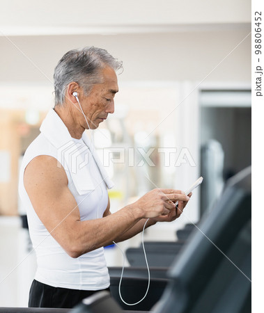音楽を楽しみながらランニングマシーンを使うシニア男性 98806452