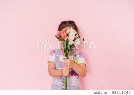 Little girl in overalls holding flowers against pink background, mother's day 98811349