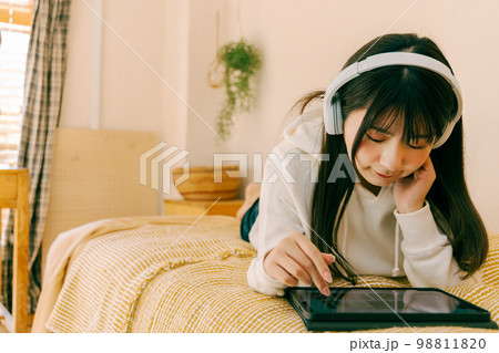 ベッドで寝そべりながら音楽を聴く若い女性 ベッドで寝そべりながら音楽を聴く若い女性 98811820