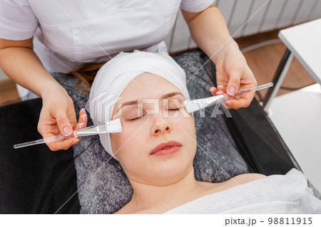 Beautician applying clay face mask on woman face. Beautician working Beautician applying clay face mask on woman face. Beautician working 98811915