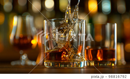 Close-up of pouring whiskey or rum on the bar, dark toned background Close-up of pouring whiskey or rum on the bar, dark toned background 98816792