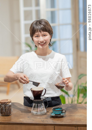 ドリッパーにコーヒー豆を入れるソムリエエプロン姿の女性スタッフ 98816873