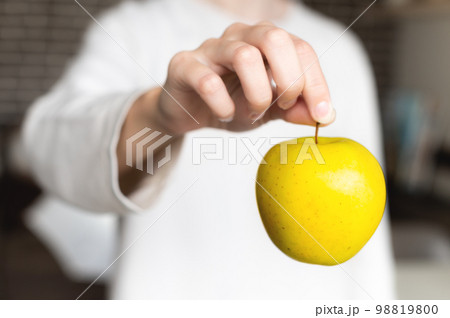 close-up, a woman's hand holds an apple by the tail hanging, the background is blurred. unrecognizable person 98819800