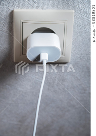 Phone charger in an electrical socket on the wall, close-up, vertical photo Phone charger in an electrical socket on the wall, close-up, vertical photo 98819801