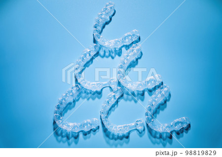 Close up, invisible aligners on a blue background in the shape of a pyramid or triangle creating a pattern. Plastic braces for teeth alignment 98819829