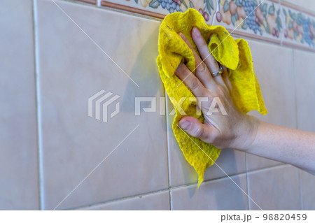 Woman's hands cleaning the tiles with a yellow rag. Space for text. Woman's hands cleaning the tiles with a yellow rag. Space for text. 98820459
