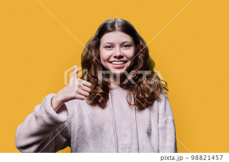 Preteen schoolgirl showing thumbs up ok sign, on yellow background 98821457