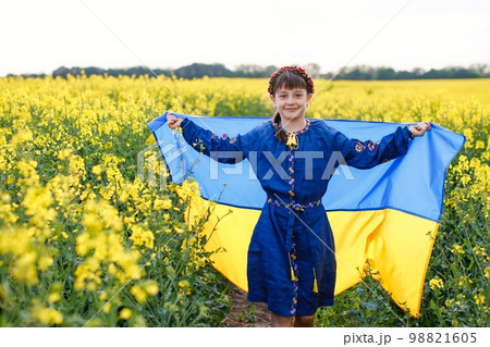 Child with Ukrainian flag in rapeseed field. A girl in an embroidered shirt runs across the field with the Ukrainian flag in her hands 98821605