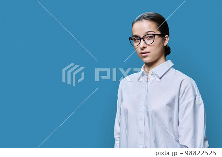 Smiling teenage female student looking at camera on blue background Smiling teenage female student looking at camera on blue background 98822525