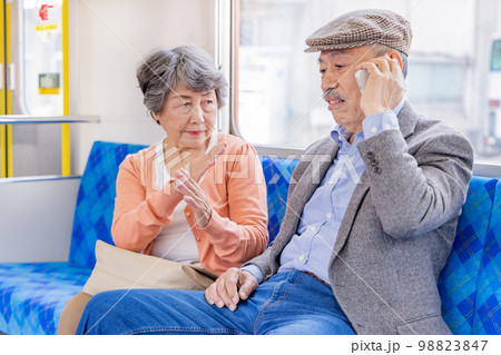 電車内　スマホで会話をする人に注意をするシニア女性 98823847
