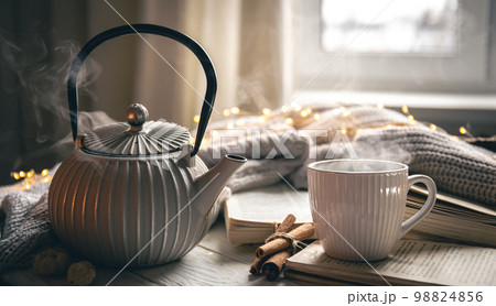 Cozy composition with a teapot, a cup and a book on a blurred background. Cozy composition with a teapot, a cup and a book on a blurred background. 98824856