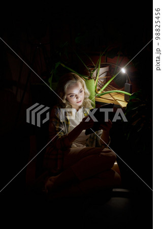 Young beautiful woman sitting in dark room sitting on chair with laptop at home in the evening with battery powered lamp light. No electricity, blackout Young beautiful woman sitting in dark room sitting on chair with laptop at home in the evening with battery powered lamp light. No electricity, blackout 98825456