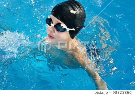 Preschool boy learning how to swim in a pool wearing swimming cap and goggles 98825860