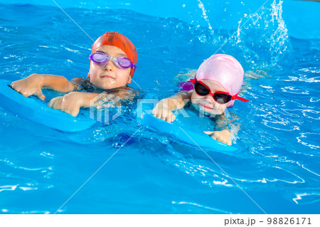 Two little girls having fun in pool learning how to swim using flutter boards Two little girls having fun in pool learning how to swim using flutter boards 98826171