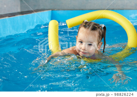 Preschool girllearning to swim in pool with foam noodle with young trainer 98826224