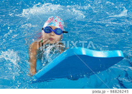 Little girl learning to swim in indoor pool with pool board Little girl learning to swim in indoor pool with pool board 98826245