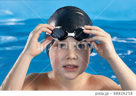 Preschool boy learning how to swim in a pool wearing swimming cap and goggles Preschool boy learning how to swim in a pool wearing swimming cap and goggles 98826258
