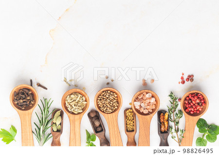 Various spices and green herbs in wooden spoons on white table 98826495