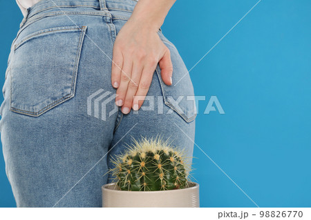 Woman sitting down on cactus against light blue background, space for text. Hemorrhoid concept 98826770