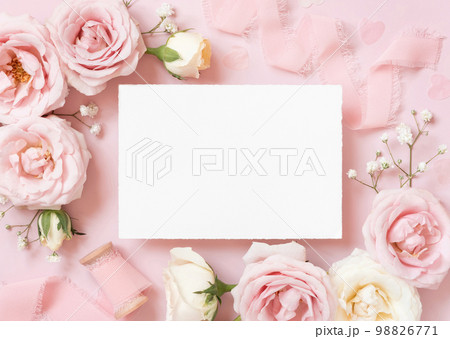 Blank paper card between pink roses and pink silk ribbons on pink top view, wedding mockup Blank paper card between pink roses and pink silk ribbons on pink top view, wedding mockup 98826771