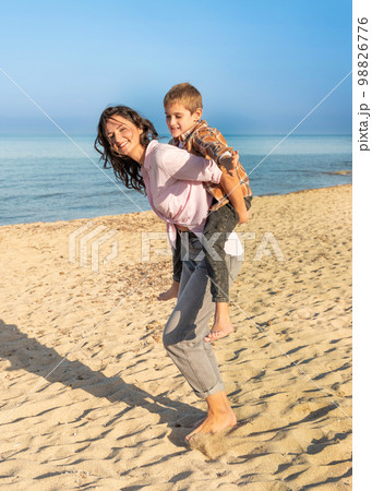 Happy Mother and son running and playing on beach barefoot, sunny day near the sea Happy Mother and son running and playing on beach barefoot, sunny day near the sea 98826776