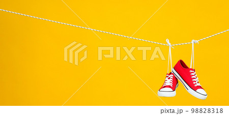 Pair of red sneakers hanging on twine on yellow background Pair of red sneakers hanging on twine on yellow background 98828318