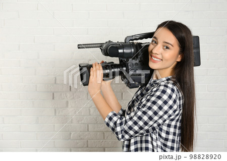 Operator with professional video camera near white brick wall Operator with professional video camera near white brick wall 98828920