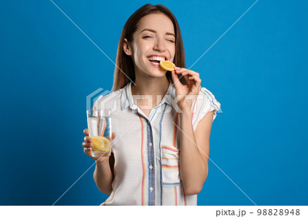 Young woman with glass of lemon water on light blue background 98828948