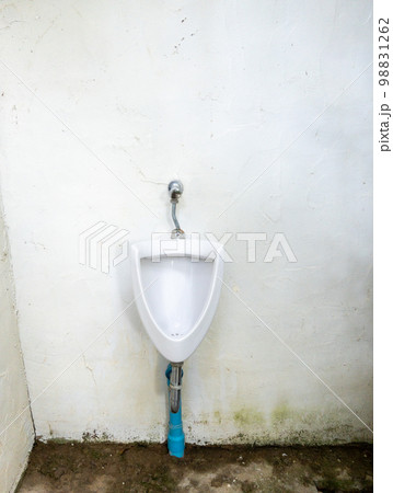 The dirty urinal of the open air toilet near the white wall. 98831262