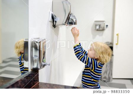 Child using restroom. Little boy dries his hands in the toilet with an automatic dryer. Taking care of the hygiene of children in public places. Healthy habits 98833350