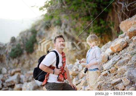 Cute schoolchild and his mature father hiking together on mountain and exploring nature. Dad and son spend quality time together.Concepts of adventure and hiking tourism 98833406