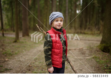 Little boy in red vest is playing with big branch and having fun in forest on early spring day. Activity for children. Outdoor recreation for family Little boy in red vest is playing with big branch and having fun in forest on early spring day. Activity for children. Outdoor recreation for family 98833449