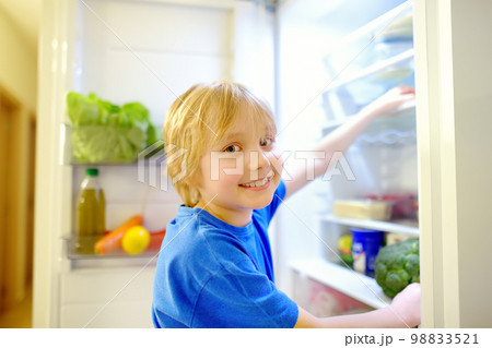 Cute preteen boy independently taking products from refrigerator at home. Child choosing between healthy and unhealthy food. Intuitive nutrition, conscious nutrition Cute preteen boy independently taking products from refrigerator at home. Child choosing between healthy and unhealthy food. Intuitive nutrition, conscious nutrition 98833521