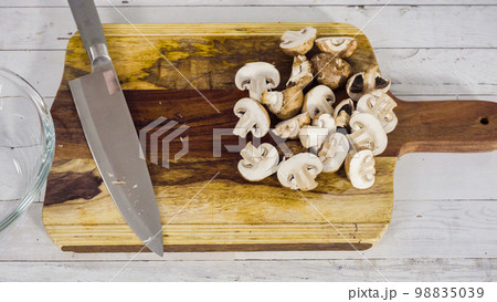 Cutting organic Bella mushrooms on a wood cutting board. 98835039
