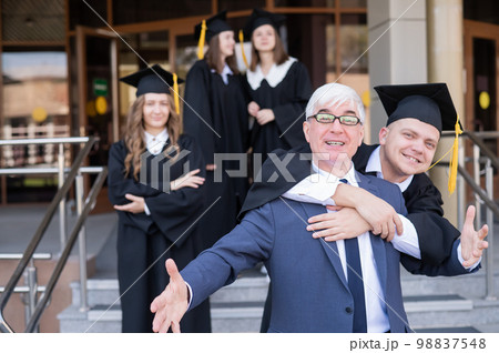 Father and son embrace at graduation. Parent congratulates university graduate. Father and son embrace at graduation. Parent congratulates university graduate. 98837548