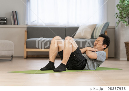 自宅のリビングで筋トレをする50代男性 98837958