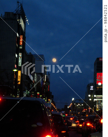 月夜の札幌すすきの交差点夜景　雪が舞う空にピンクの満月 98842521