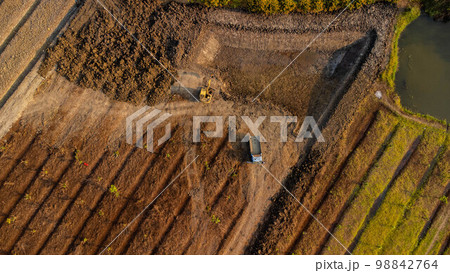 Aerial view of a wheel loader excavator with a backhoe loading sand onto a heavy earthmover at a construction site. Aerial view of a wheel loader excavator with a backhoe loading sand onto a heavy earthmover at a construction site. 98842764