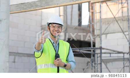 Professional engineer inspecting the construction of a house or factory building and giving a thumbs up showing readiness and good performance, Engineer's safety suit and helmet. 98845113