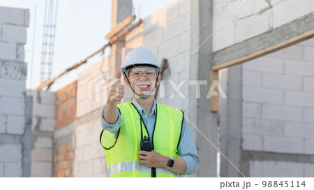 Professional engineer inspecting the construction of a house or factory building and giving a thumbs up showing readiness and good performance, Engineer's safety suit and helmet. 98845114