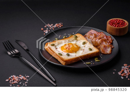 Heart shaped fried egg in bread toast with sesame seeds, flax seeds and pumpkin seeds on a black plate Heart shaped fried egg in bread toast with sesame seeds, flax seeds and pumpkin seeds on a black plate 98845320