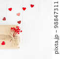 Valentine's Day flatlay. Gift box of craft paper with hearts and red flowers on the white wooden background. 98847311