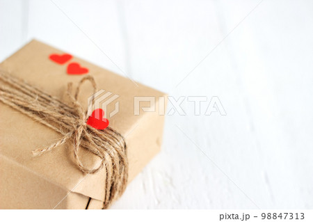 Gift box of craft paper with hearts on the white wooden background. Valentine's Day. 98847313